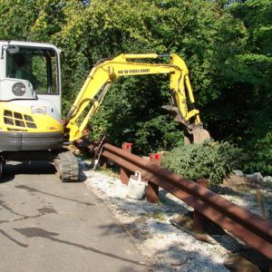 A mini-excavator machine assists with installing trees along a guard rail on Old Mill Rd. for Riverwood Condominiums.