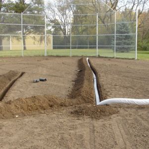 Perforated drain tile with nylon sock is laid in the trenches under the baseball field.