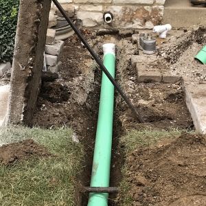 Concrete sidewalk slab lifted to allow sump pump line to be buried and run to rear of yard, away from house in Mount Pleasant, WI.