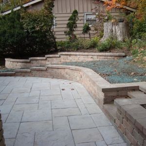 Unilock Yorkstone pavers are made to look like natural flagstone but have the consistency of concrete. Olde Quarry retaining walls were installed to maximize the space in this sloped rear yard in Greendale.