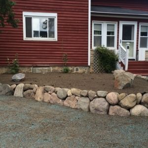 Granite boulder wall installed to create raised planting bed along side of farm house in Franksville.