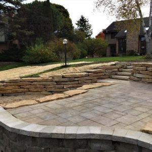 Lake side patio made of County Materials Grand Discover pavers (Timeless color). Patio built between tiered outcropping stone walls.