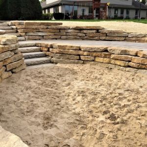 Retaining Walls made of rustic gold outcropping stone with Rosetta pre-cast steps and Unilock paver patio. Installation in Mount Pleasant, WI.