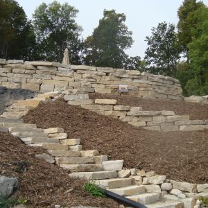 Rustic gold lannon outcropping stone tiered retaining wall along with steps and inset paver patio, provides erosion control and aesthetic access to Lake Michigan shoreline in Wind Point.