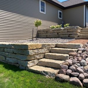 Two tiered Rustic Gold Outcropping stone retaining wall and steps installed on sloped side yard in Caledonia
