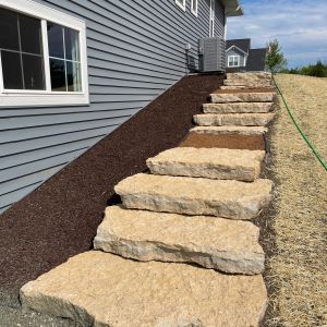 Rustic gold outcropping stone steps with brown granite landings installed down to walk out basement in Caledonia, WI.